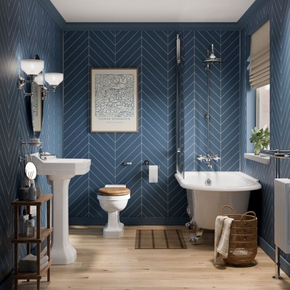 Lifestyle image of the Showerwall Laminate Nordic Blue 2400mm x 600mm Chevron Tile Effect Wall Panel - SWT15 installed across an entire traditional bathroom with toilet, rolltop bathtub and pedestal basin with wall lights
